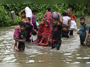 People carry their belongings and wade through flooded water to reach a temporar...