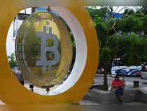 A woman sits by a Bitcoin sign at the Bitcoin Plaza, in Ilopango