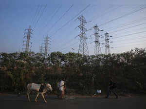 A man walks his cow under high-tension power lines leading from a Tata Power sub station in Mumbai's suburbs