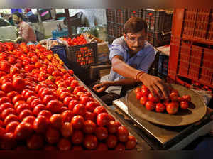 A vendor weights tomatoes for a customer at a vegetable market in Ahmedabad