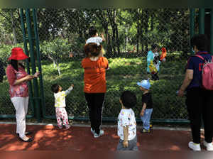 Children play next to adults at a park in Beijing