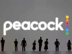 Toy figures of people are seen in front of the displayed Peacock logo, in this illustration