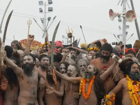 Naga Sadhus covered in ash with swords in hand prepares to take a dip during the Maha Kumbh Mela