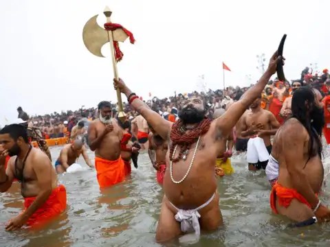 A Naga Sadhu or Hindu holy man holds an axe as he takes a holy dip during the Maha Kumbh Mela