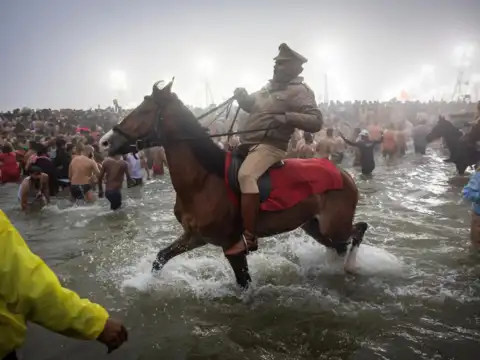 Policemen on horses remove devotees from the water before the arrival of Naga Sadhus before the first Shahi Snan