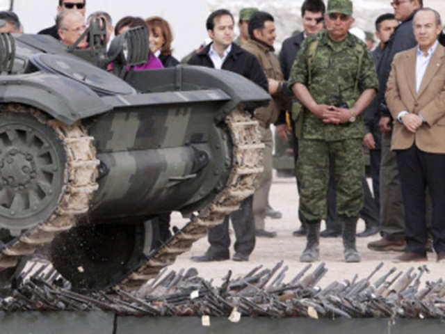 Mexican President Calderon looks as a tank destroys weapons seized from drug traffickers