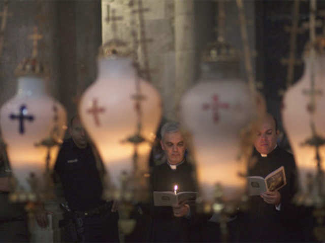 Catholic priests pray beside the Stone of Anointing
