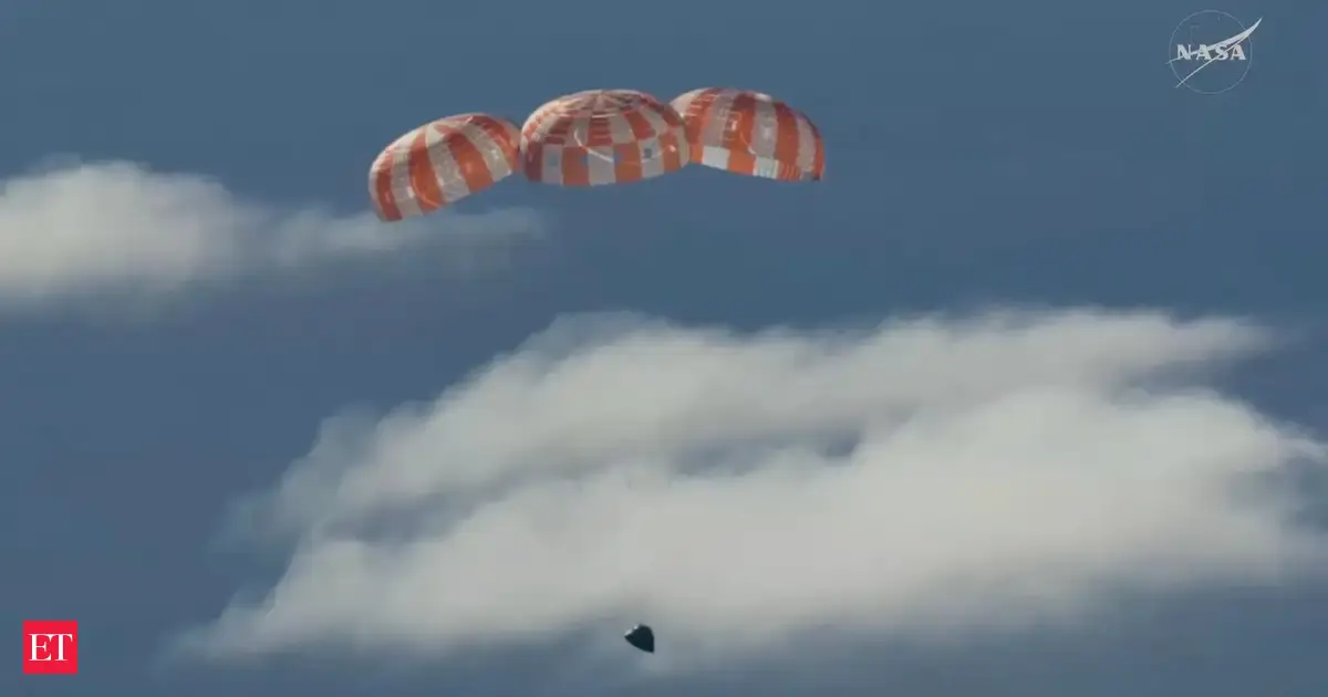 Artemis II Orion capsule floating in the ocean after splashdown, with recovery teams approaching.