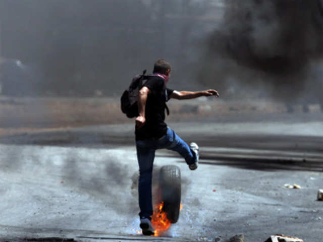 A Palestinian youth kicks a flaming tire during clashes with Israeli soldiers