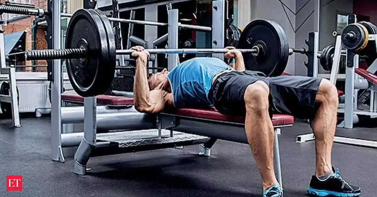 A person sniffing a dark chocolate bar in a gym setting, with weights in the background.