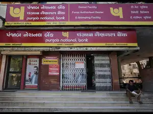 A man reads a newspaper outside a branch of Punjab National Bank in Ahmedabad