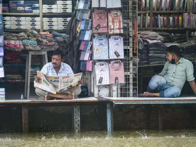 Mumbai: Shopkeepers sit in their shops on a waterlogged street at Hindmata in Mu...