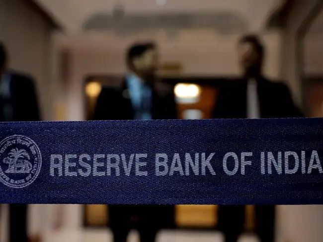 FILE PHOTO: A Reserve Bank of India (RBI) logo as people stand in the background, ahead of a press conference, after a monetary policy review in Mumbai, India, August 5, 2026.