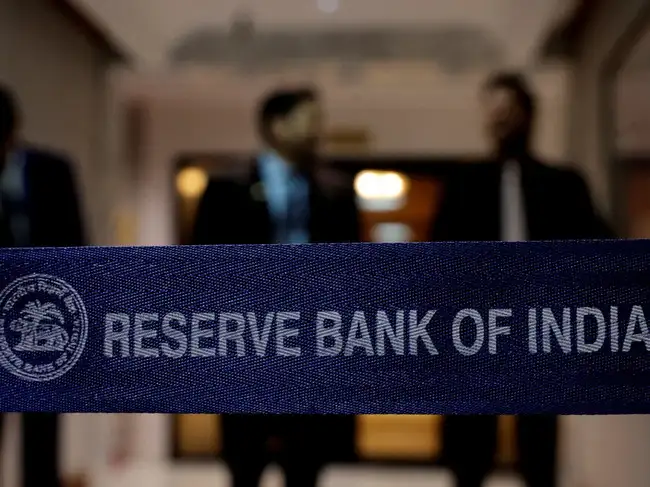 FILE PHOTO: A Reserve Bank of India (RBI) logo as people stand in the background, ahead of a press conference, after a monetary policy review in Mumbai, India, August 5, 2026.