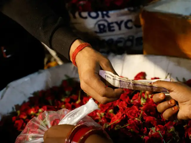 A vendor hands a currency note to a customer at a wholesale market in New Delhi