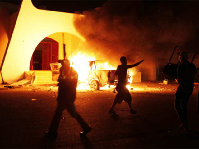 Demonstrators carrying guns celebrate after burning a car as they stormed the headquarters of the Islamist Ansar al-Sharia militia group in Benghazi