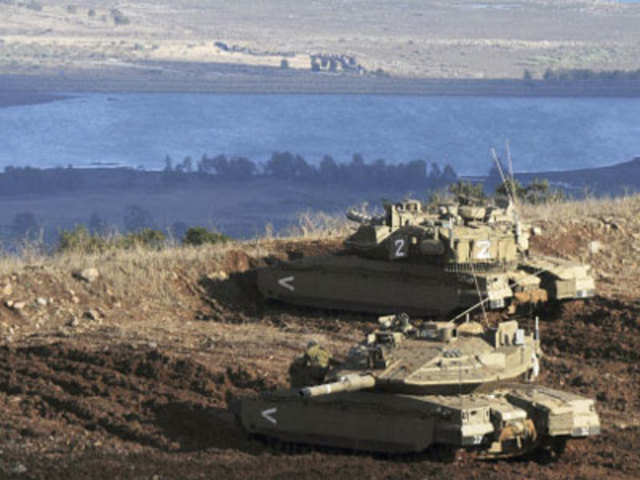 Israeli tanks stand in position overlooking a Syrian village