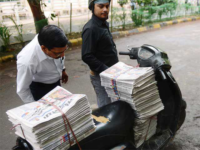 An aam admi reads newspaper on a deliveryman's scooter in Delhi