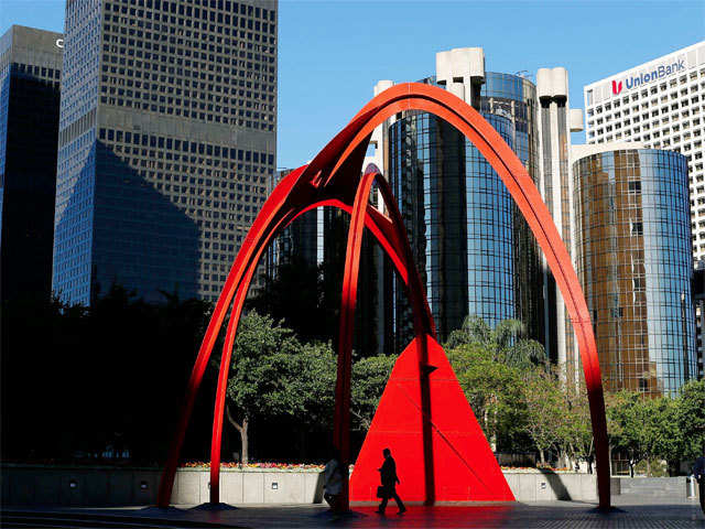 A businessman checks his phone as he walks past a sculpture in downtown Los Angeles