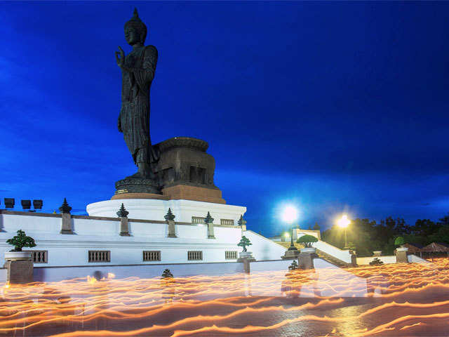 Buddhists holding candles encircle a large Buddha statue during Vesak Day in Nakhon Pathom province