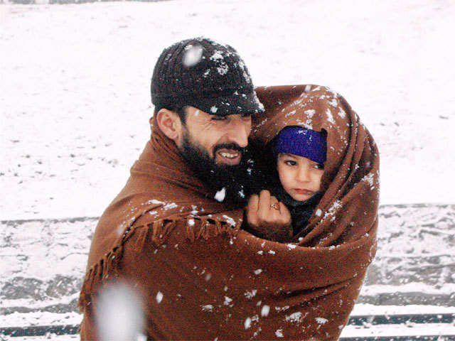 A man wraps his child in a shawl in Anantnag