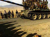 Northern Alliance fighters ride on a T-62 tank past a dead body