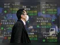 FILE PHOTO: A man walks past an electronic board showing the stock market indices of various countries outside a brokerage in Tokyo