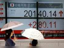 FILE PHOTO: Women holding parasols, look at an electronic board showing Japan's Nikkei average outside a brokerage in Tokyo