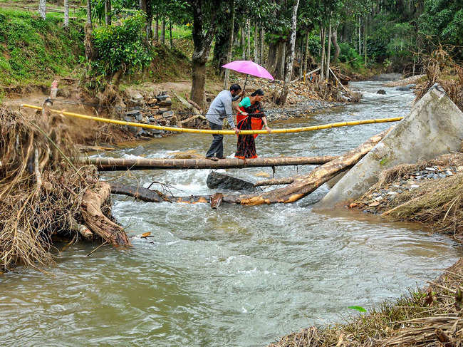 Residents cross a stream using a temporary bridge after the connecting bridge was washed away in flood waters near Mudigere in Chikmagalur district. (PTI)​