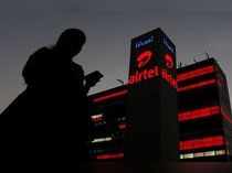 A girl checks her mobile phone as she walks past the Bharti Airtel office building in Gurugram