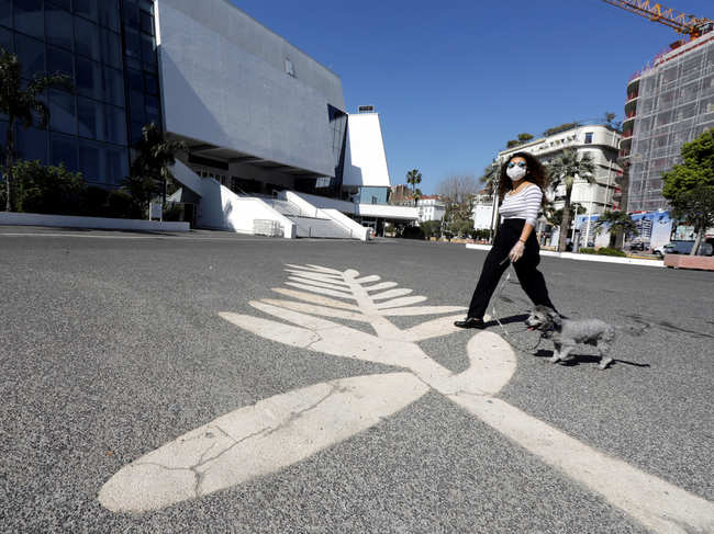 A woman wearing a face mask walks her dog past a Palme d'Or symbol on the pavement near the Festival palace on the Croisette in Cannes where the Cannes Film Festival and the Cannes Lions take place, as a lockdown is imposed to slow the rate of the coronavirus disease (COVID-19), in France, March 18, 2020.