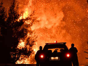Firefighters stand near a pine forest wildfire fanned by strong winds near the village of Athikia, in Peloponnese area near Corinth late on July 22, 2020 AFP
