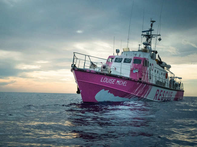 Painted in bright pink, the vessel features Banksy artwork depicting a girl in a life vest holding a heart-shaped safety buoy.
