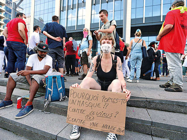 A woman holds a placard saying, "Why do you wear mask? Against the virus or to avoid a e250 fine?" during a demonstration against the sanitary measures taken by Belgium