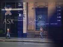 Pedestrians are reflected in a window in front of a board displaying stock prices at the Australian Securities Exchange in Sydney