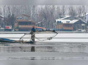 Srinagar: A fisherman throws a net to catch fish in snow covered Dal Lake after ...