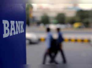 FILE PHOTO: Commuters walk past a bank sign along a road in New Delhi