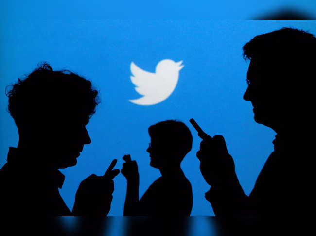 FILE PHOTO: Smartphone users are silhouetted against a backdrop projected with the Twitter logo