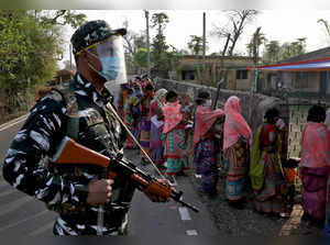 An armed policeman wearing a face shield stands guard as women wait in line to cast their votes outside a polling booth during the first phase of the West Bengal state election in Purulia