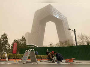 Construction workers are seen in front of the CCTV headquarters shrouded in dust as the city is hit by a sandstorm, in Beijing