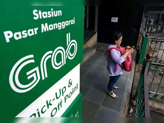 A woman uses her phone near a sign for the online ride-hailing service Grab at the Manggarai train station in Jakarta