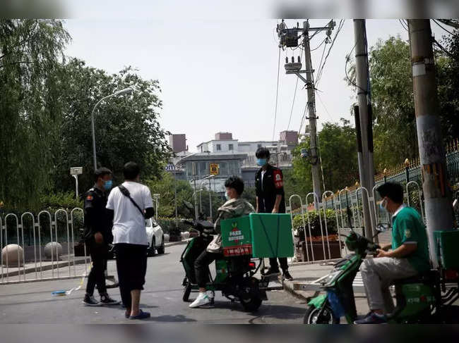 Security personnel and delivery workers are seen at an entrance to a residential area in Beijing