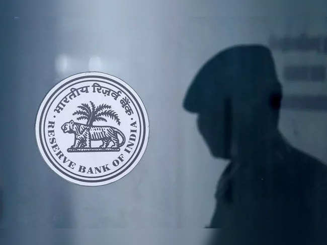 A security guard's reflection is seen next to the logo of the Reserve Bank Of India (RBI) at the RBI headquarters in Mumbai