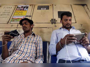Commuters watch videos on their mobile phones as they travel in a suburban train in Mumbai