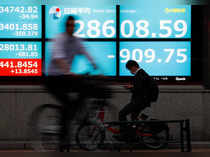 People ride bicycles past a screen displaying Nikkei share average outside a brokerage in Tokyo
