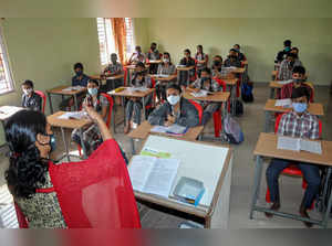 Chikmagalur: Students of the 10th class, wearing masks, attend a class at a scho...