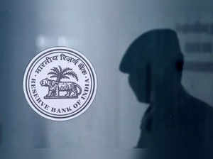 A security guard's reflection is seen next to the logo of the Reserve Bank Of India (RBI) at the RBI headquarters in Mumbai