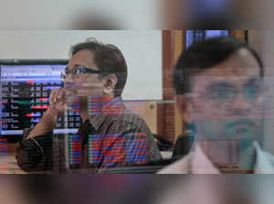 A broker watches a TV news channel as another monitors share prices at a brokerage firm in Mumbai