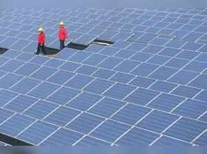 Workers walk past solar panels at a solar farm.