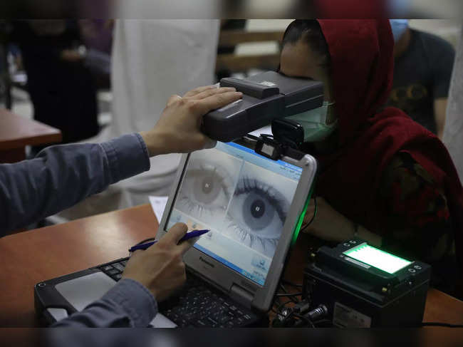 An employee scans the eyes of a woman for biometric data needed to apply ...